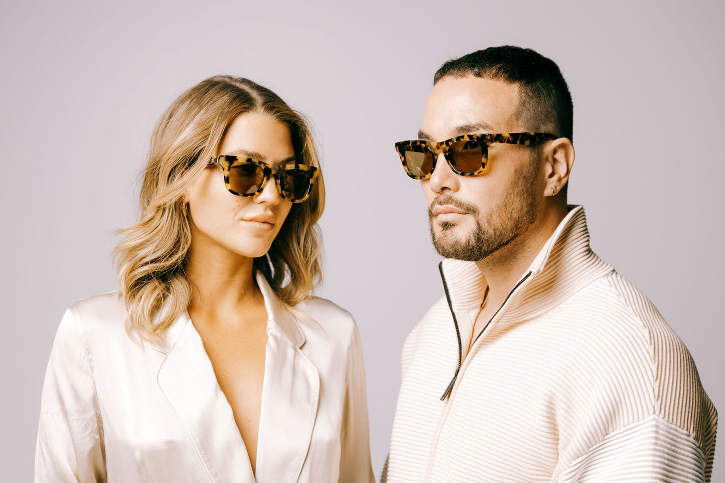 Woman and man in cream coloured clothing both wear brown tortoiseshell biodegradable and sustainable sunglasses with tan lens