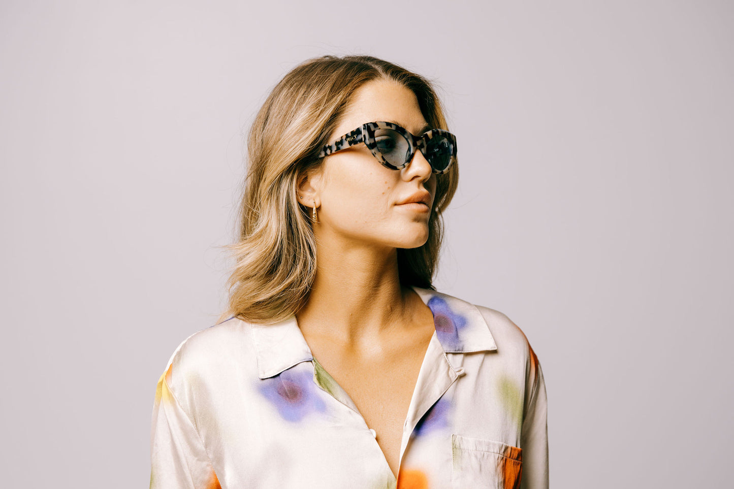 Woman in colourful silk shirt wears light tortoiseshell cateye sustainable and biodegradable Cleo Quinoa Blue sunglasses with light blue lens
