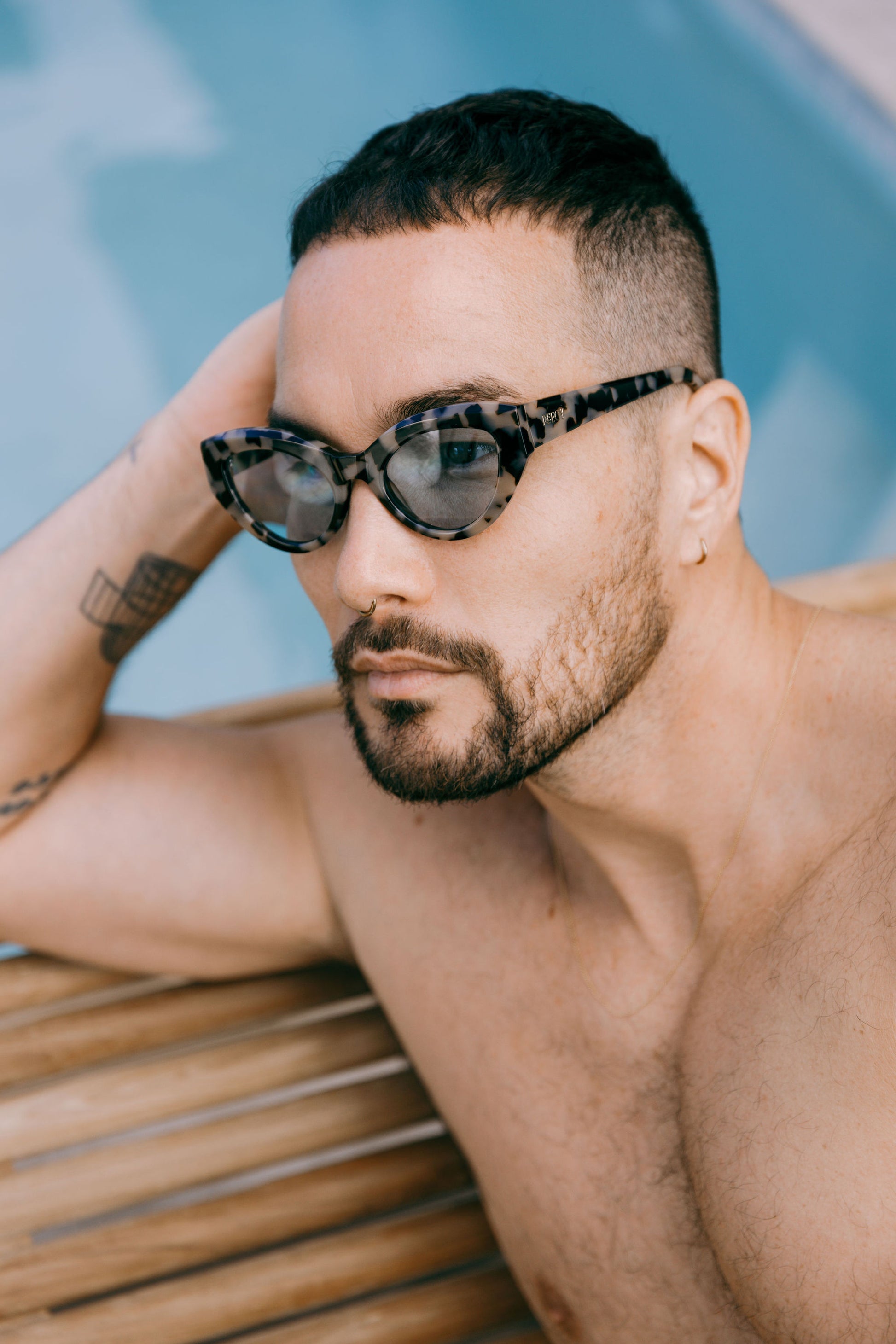 Man by a swimming pool wears light tortoiseshell cateye sustainable and biodegradable Cleo Quinoa Blue sunglasses with light blue lens